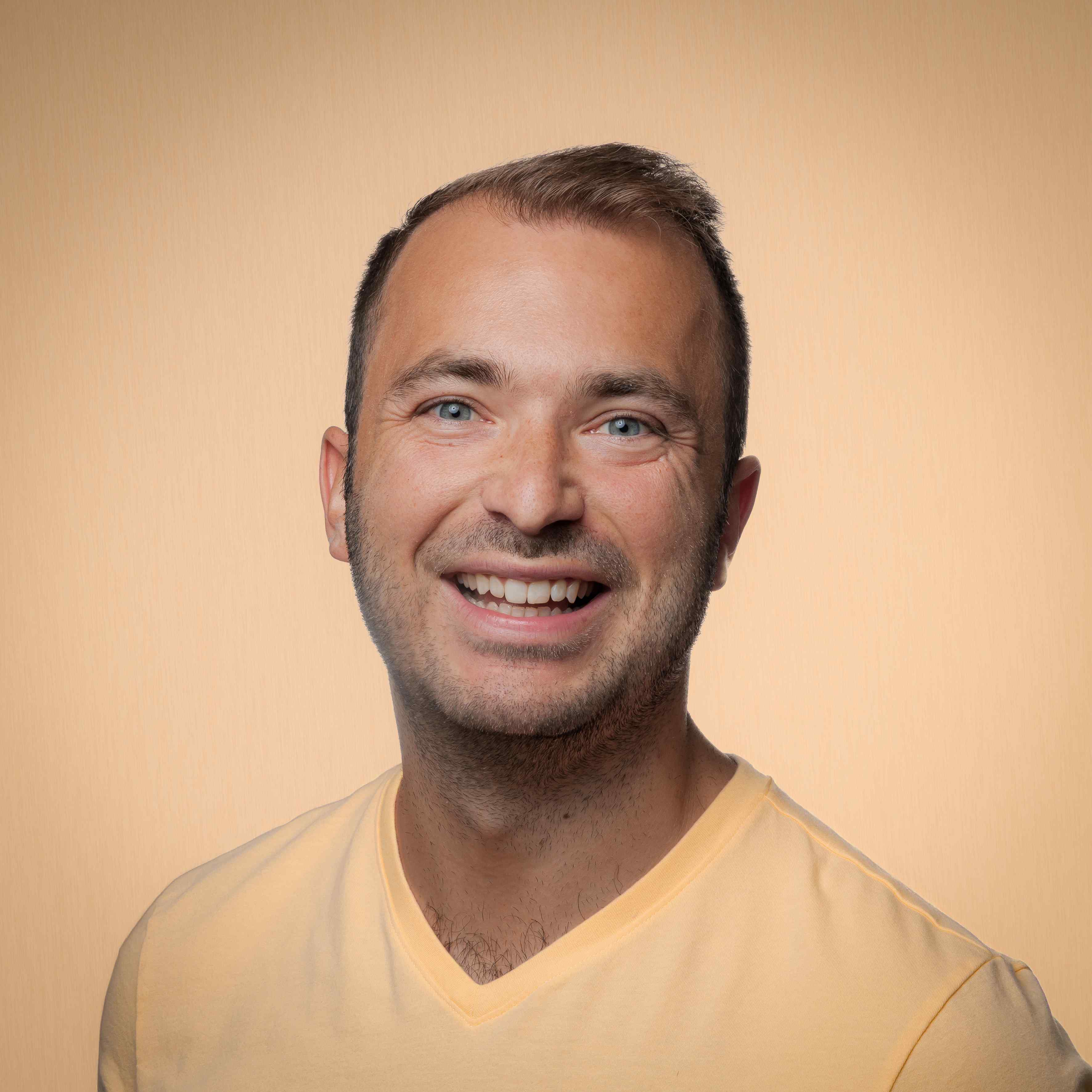 Professional headshot of Billy Hardiman with warm yellow studio background
