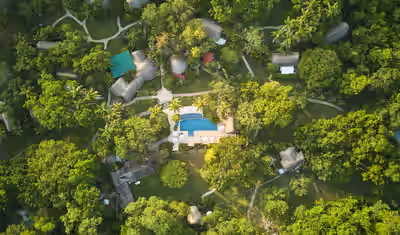 Aerial view of jungle eco‑resort with pool and network of thatched cottages at The Lodge at Chaa Creek, Belize