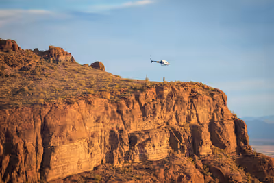 Airbus H125 helicopter flying over Arizona cliffs in morning light near Phoenix