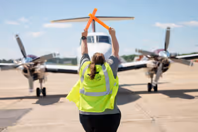 Ground marshal in safety vest directing Beechcraft King Air 200 with marshalling wands at Shreveport Regional Airport