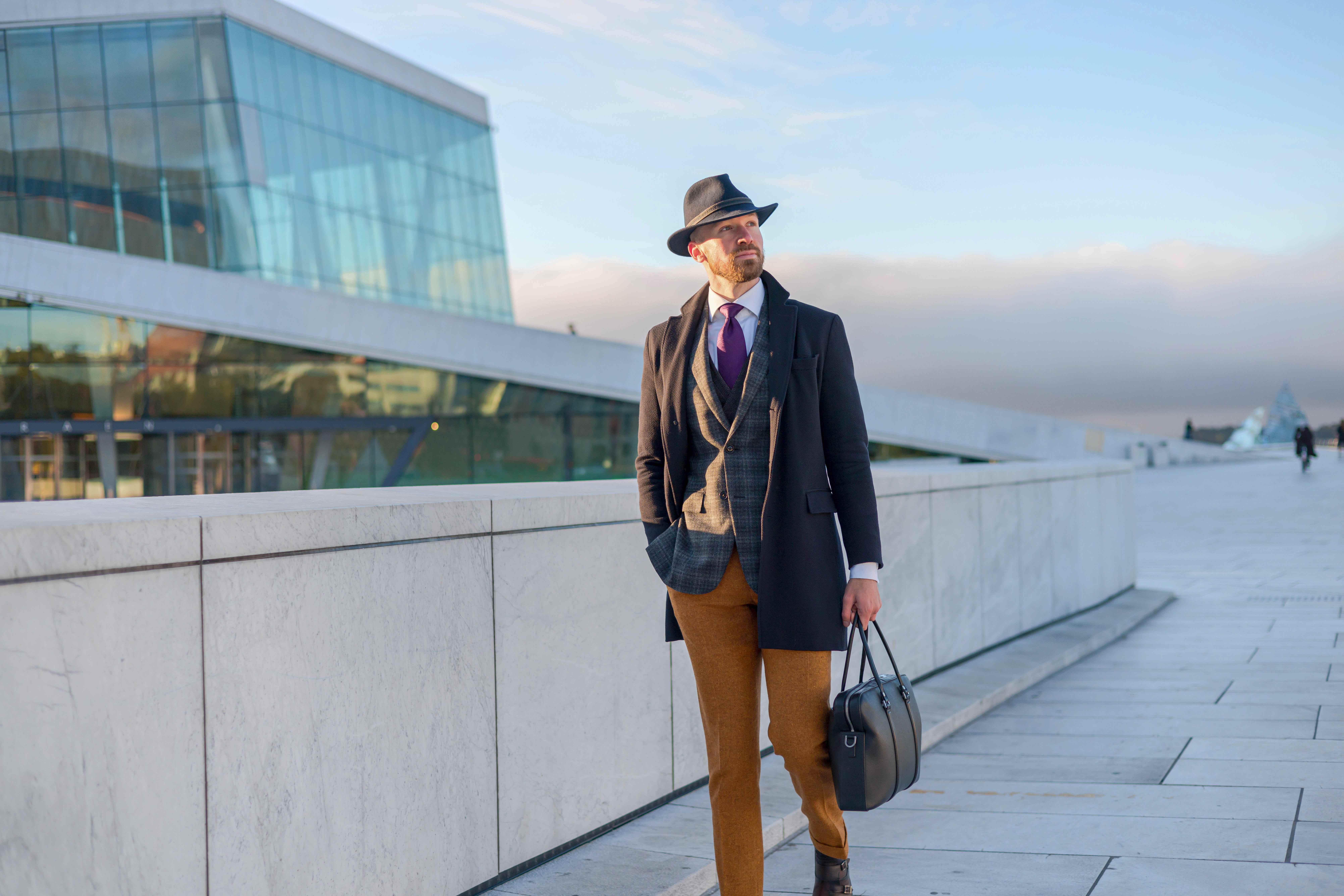 Man in stylish business attire walking near Oslo Opera House with briefcase
