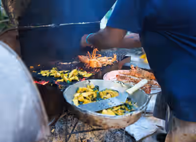 Cook grilling lobster and vegetables over charcoal at a backyard restaurant in Caye Caulker, Belize