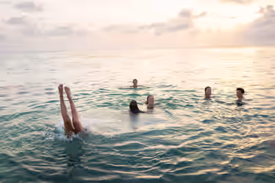 People swimming at sunset in the Caribbean Sea with one person mid-dive and legs above the water in Caye Caulker, Belize