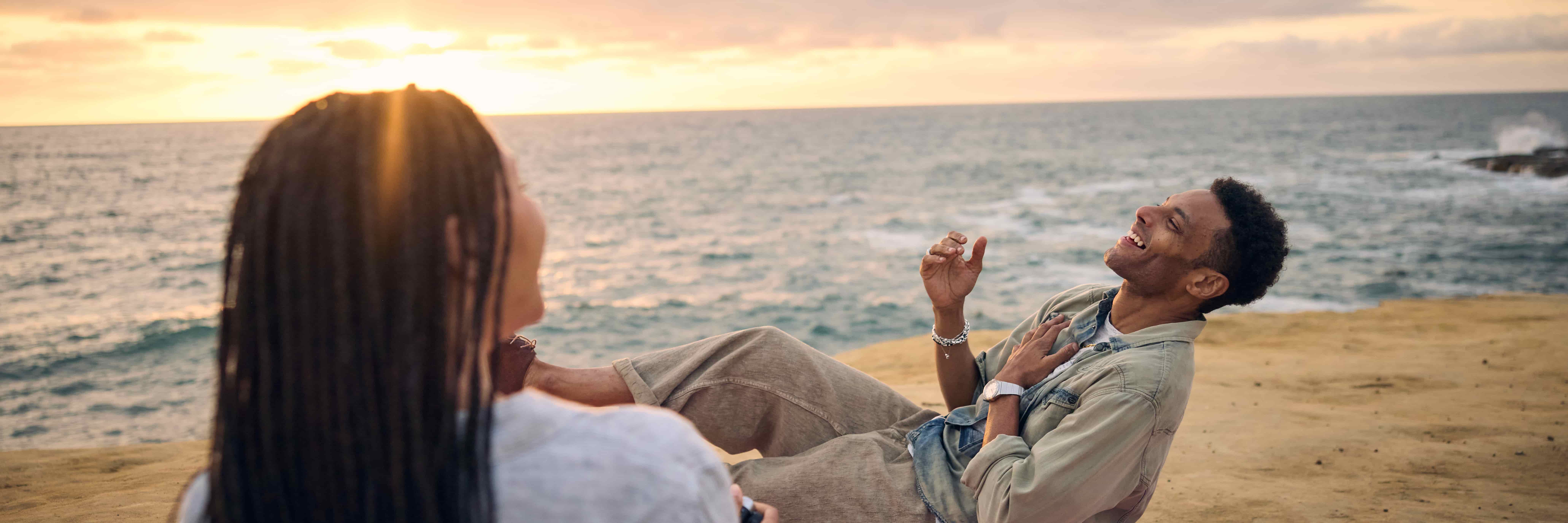 Couple laughing together on a picnic blanket beside the ocean at sunset