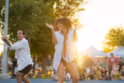 Woman dancing joyfully in front of a crowd at sunset during an outdoor event in Tempe, Arizona