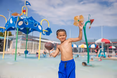 Boy playing with football in zero entry splash pool at Escalante Pool in Tempe, Arizona