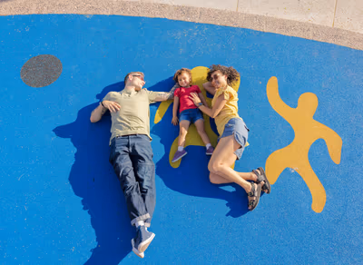 Family of three lying together on colorful rubber playground surface at a public park in Tempe, Arizona