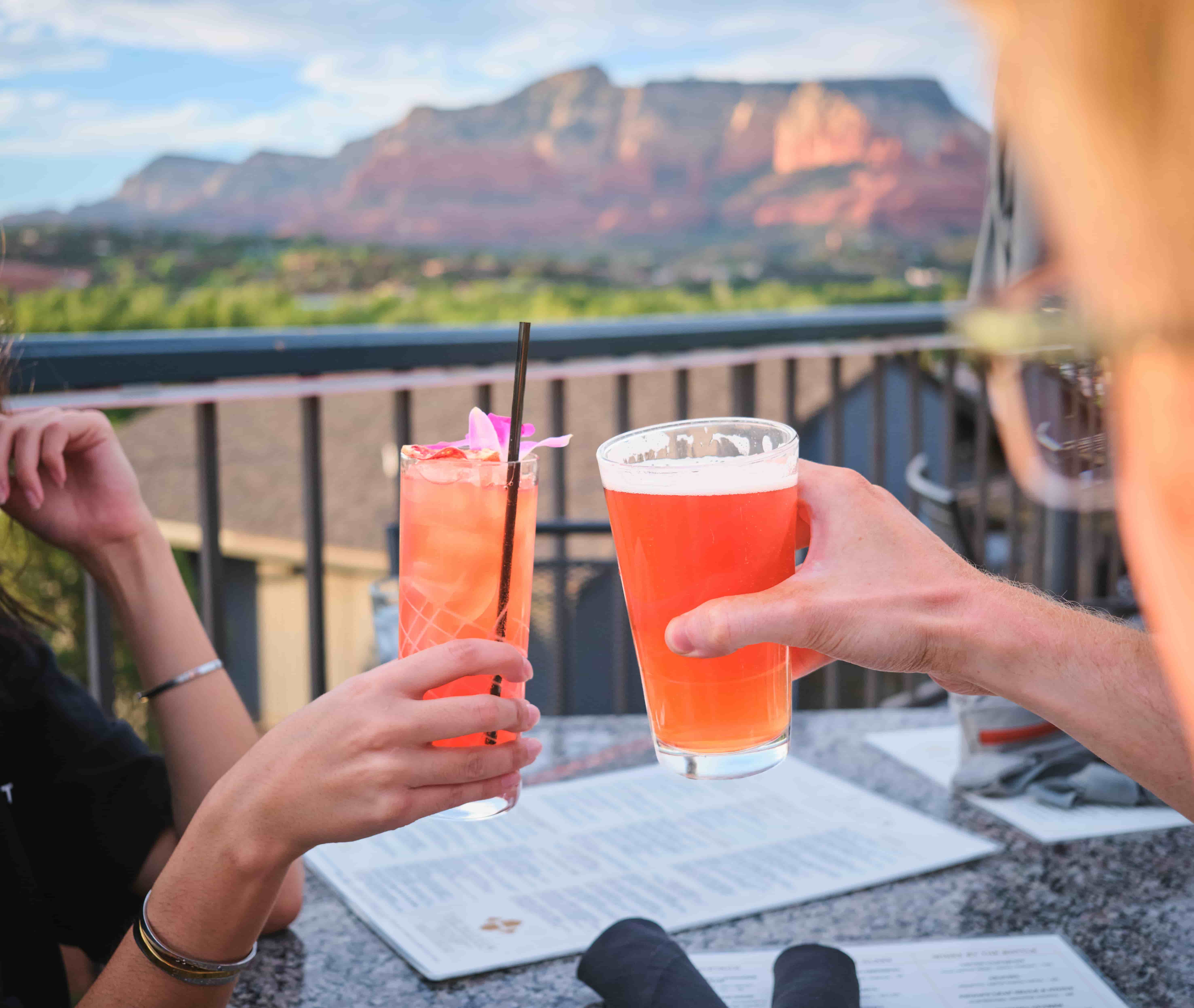 Friends toast with cocktail and beer at The Hudson, Sedona, Arizona Friends clinking a pink cocktail and beer on The Hudson's patio at sunset