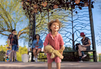 Smiling girl holding stuffed toy in front of decorative bus stop with family and skateboarder in Tempe, Arizona
