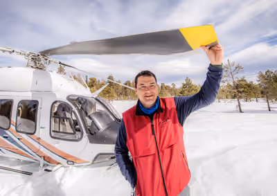 Pilot standing beside Bell 429 helicopter after landing in snow-covered field in eastern Arizona