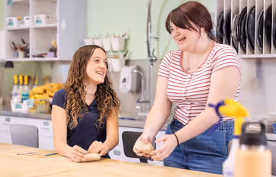 Two high school students smiling and shaping clay during pottery class in an art room