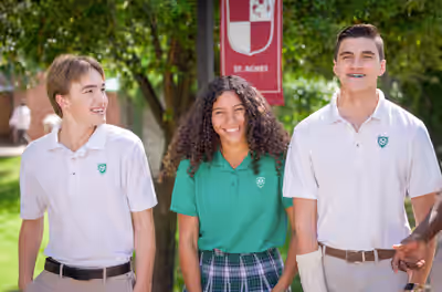 Three high school students in uniform laughing and walking together