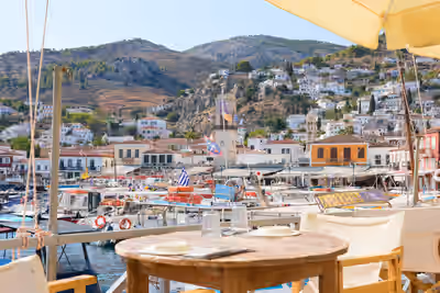 Harbor view from dining table with boats and hillside houses in Hydra, Greece