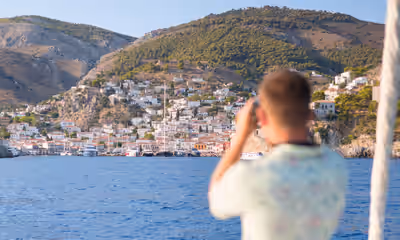 Tourist photographing hillside village from boat on Hydra island Greece