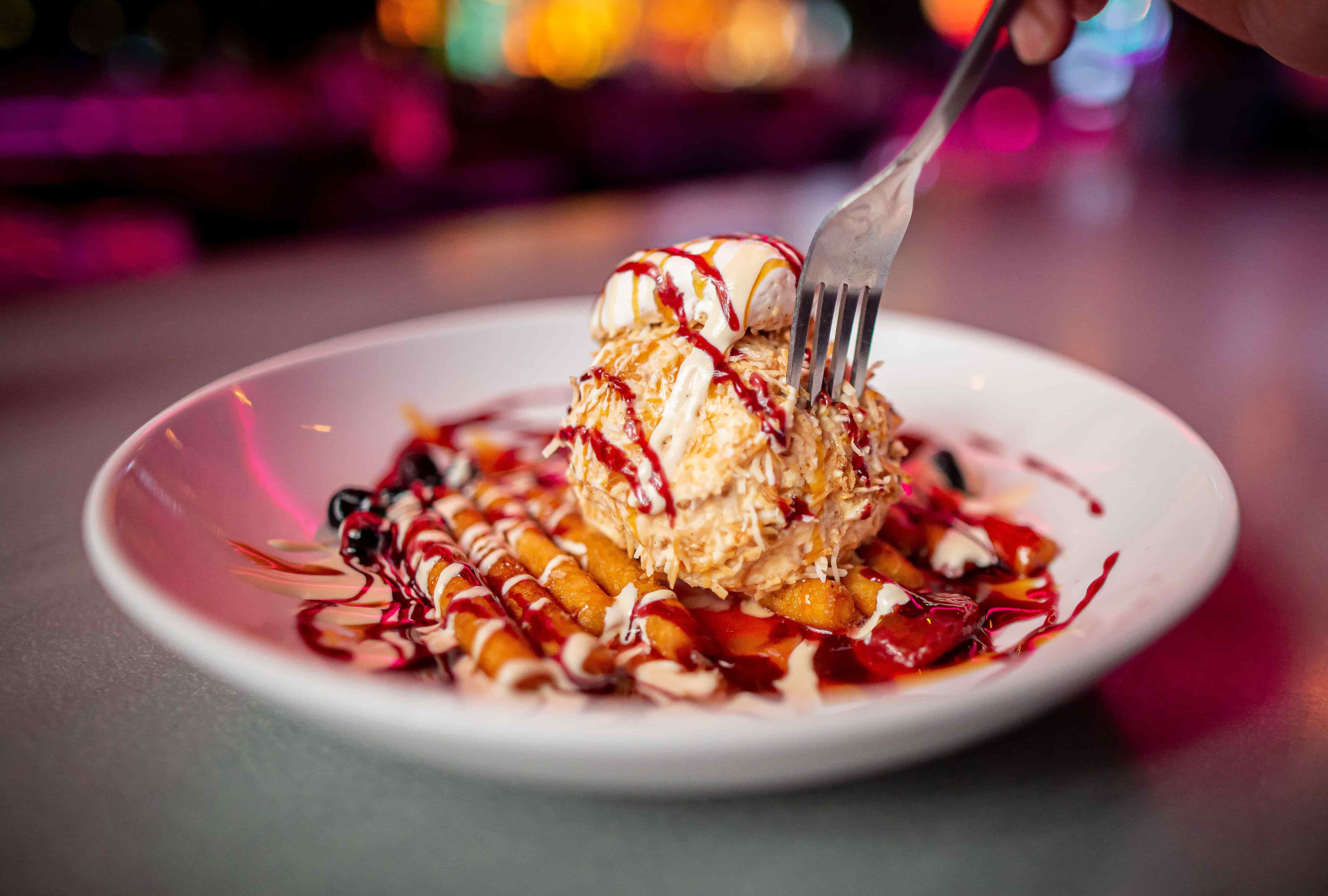 Layered dessert with fork and berry sauce in colorful restaurant light Fork cutting into a layered dessert with cream, berries, and sauce