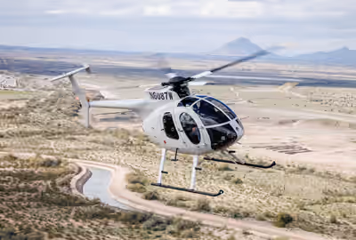 Banking MD530F helicopter flying over sparse terrain and canal near Phoenix, Arizona