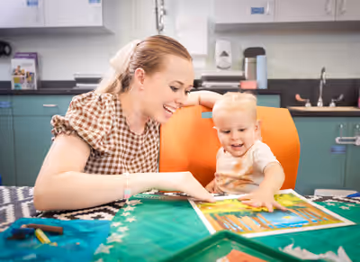 Mother and toddler smiling while doing a finger painting activity together in a classroom
