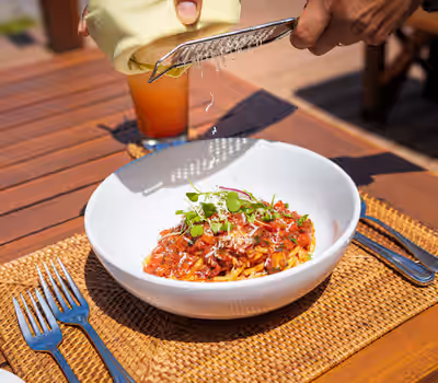 Waiter grating Parmesan cheese over pasta dish