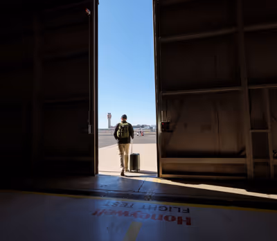 Man with suitcase walking through airport hangar door toward ramp with control tower visible at Phoenix Sky Harbor International Airport