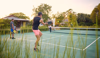Man playing pickleball at resort court with tropical trees in Placencia, Belize