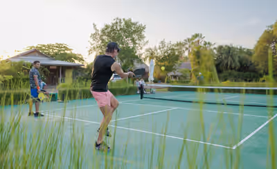 Man playing pickleball at resort court with tropical trees in Placencia, Belize