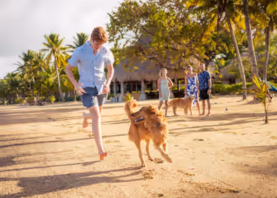 Boy running with dog on beach at sunset with family watching in Placencia Belize