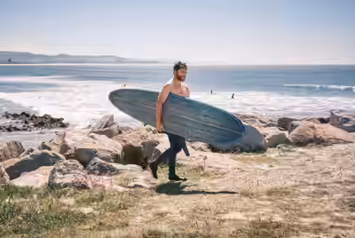 Surfer carrying longboard along rocky coastline with ocean in background