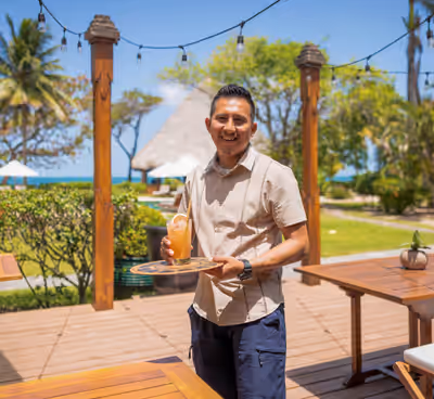 Server holding tropical drink at beachfront resort restaurant at Turtle Inn in Belize
