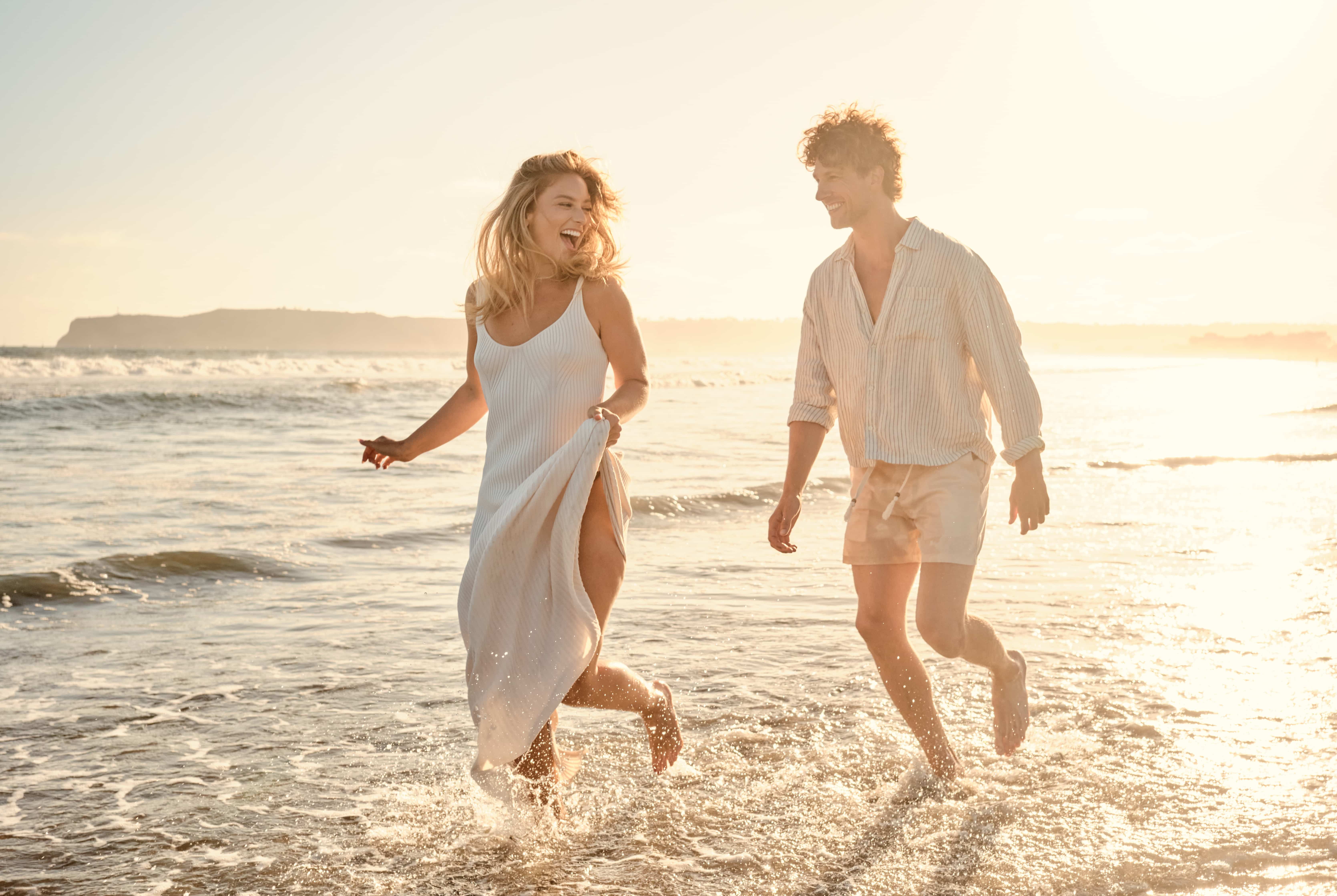 Woman looking back as she leads her partner through the surf at sunset