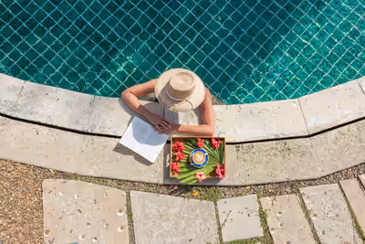Woman reading a book beside a resort pool in Belize with a tray holding a latte and tropical flowers