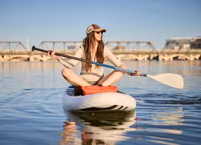 Woman paddleboarding on Tempe Town Lake with historic train bridge behind