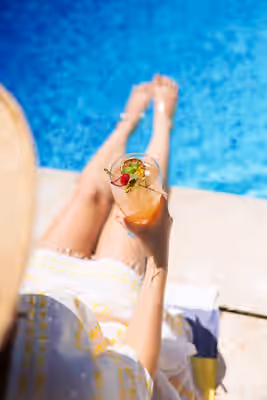 Close-up of a woman in a sundress holding a tropical cocktail while relaxing beside a swimming pool at a luxury resort