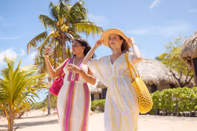 Two women in embroidered sundresses walk beside beachfront resort villas in Belize, enjoying ocean views and warm tropical weather