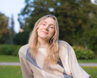 Young woman with seed pod balanced on nose smiling in Vērmanes Garden in Riga, Latvia